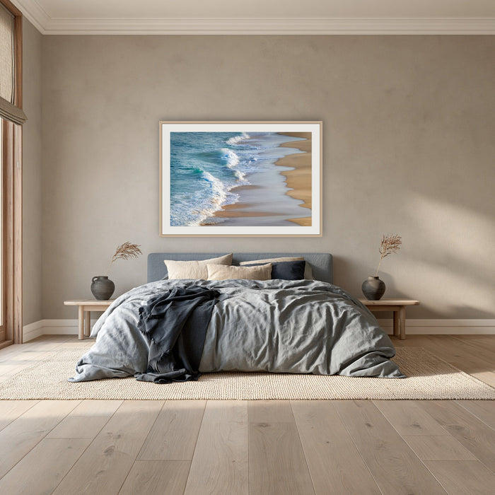 Tura Beach Waves framed print in oak with a white mat, above a dusty blue linen bed in a bedroom