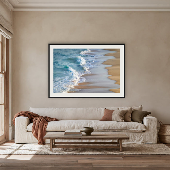 Tura Beach Waves framed print in black with a white mat, above an oatmeal linen sofa in a lounge room