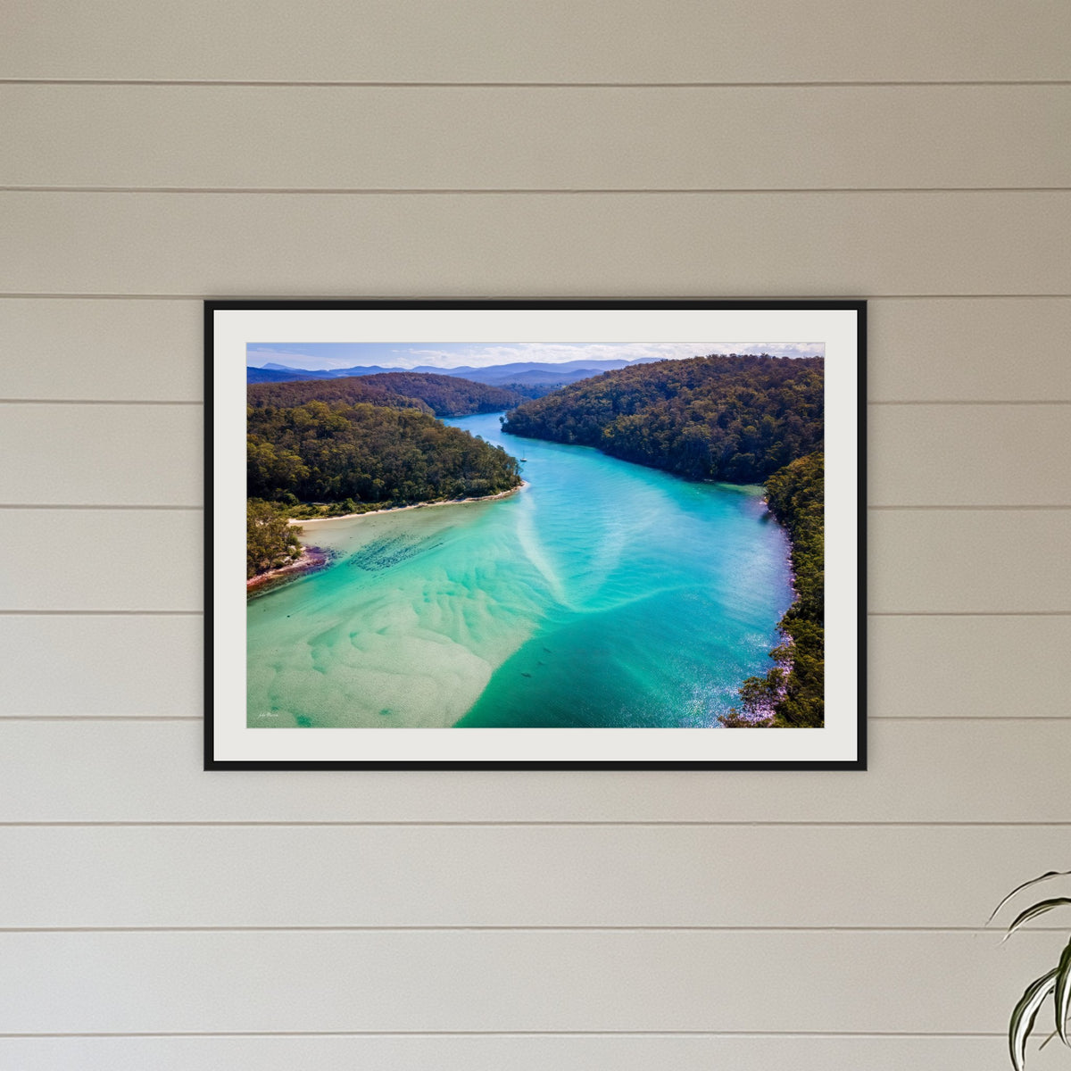 Pambula River to the Mountains framed print in black with a white mat, above a sofa