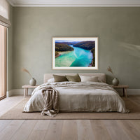 Pambula River to the Mountains framed print in oak with a white mat, above a linen bed against a sage wall in a bedroom