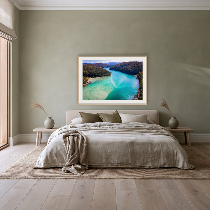 Pambula River to the Mountains framed print in oak with a white mat, above a linen bed against a sage wall in a bedroom
