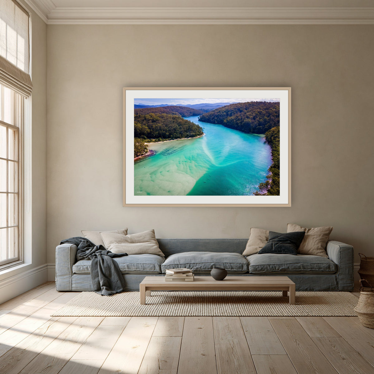 Pambula River to the Mountains framed print in oak with a white mat, above a dusty blue linen sofa in a lounge room