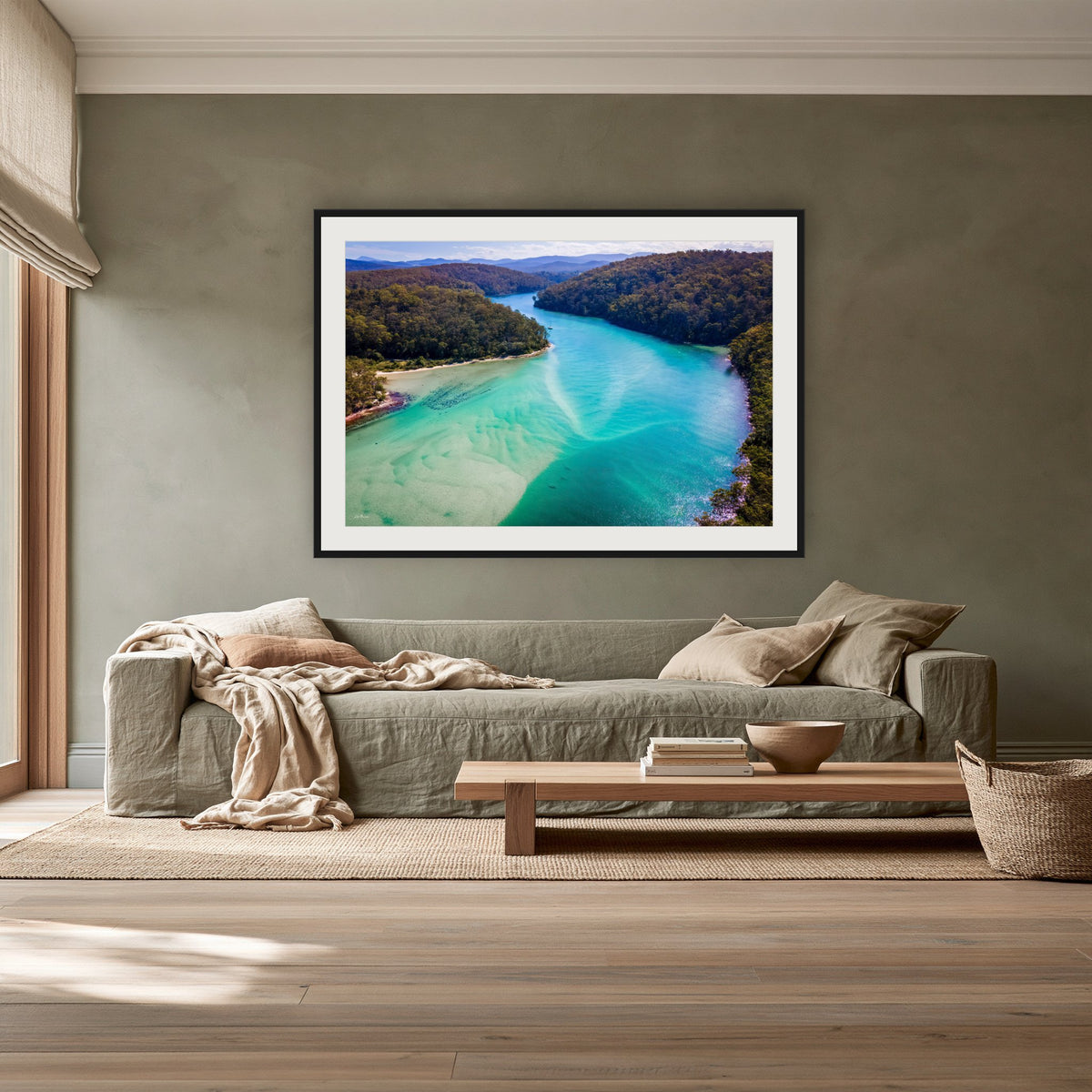 Pambula River to the Mountains framed print in black with a white mat, above a sage linen sofa in a lounge room