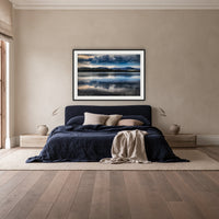 Storm Clouds over Top Lake framed print in black with a white mat, above a navy linen bed in a bedroom
