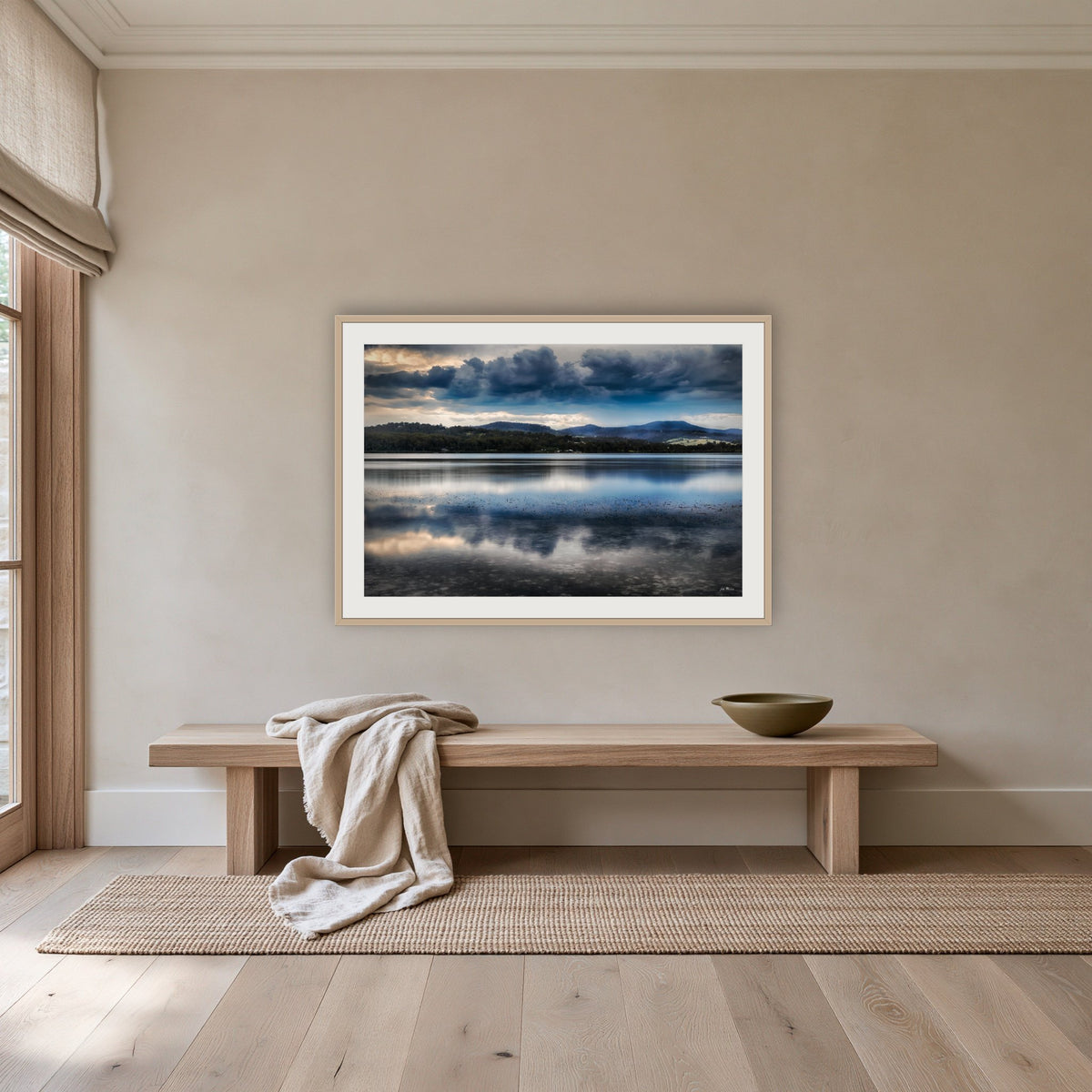 Storm Clouds over Top Lake framed print in oak with a white mat, above an oak bench in a hallway