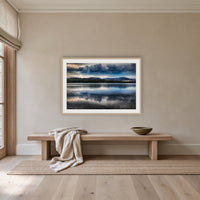 Storm Clouds over Top Lake framed print in oak with a white mat, above an oak bench in a hallway