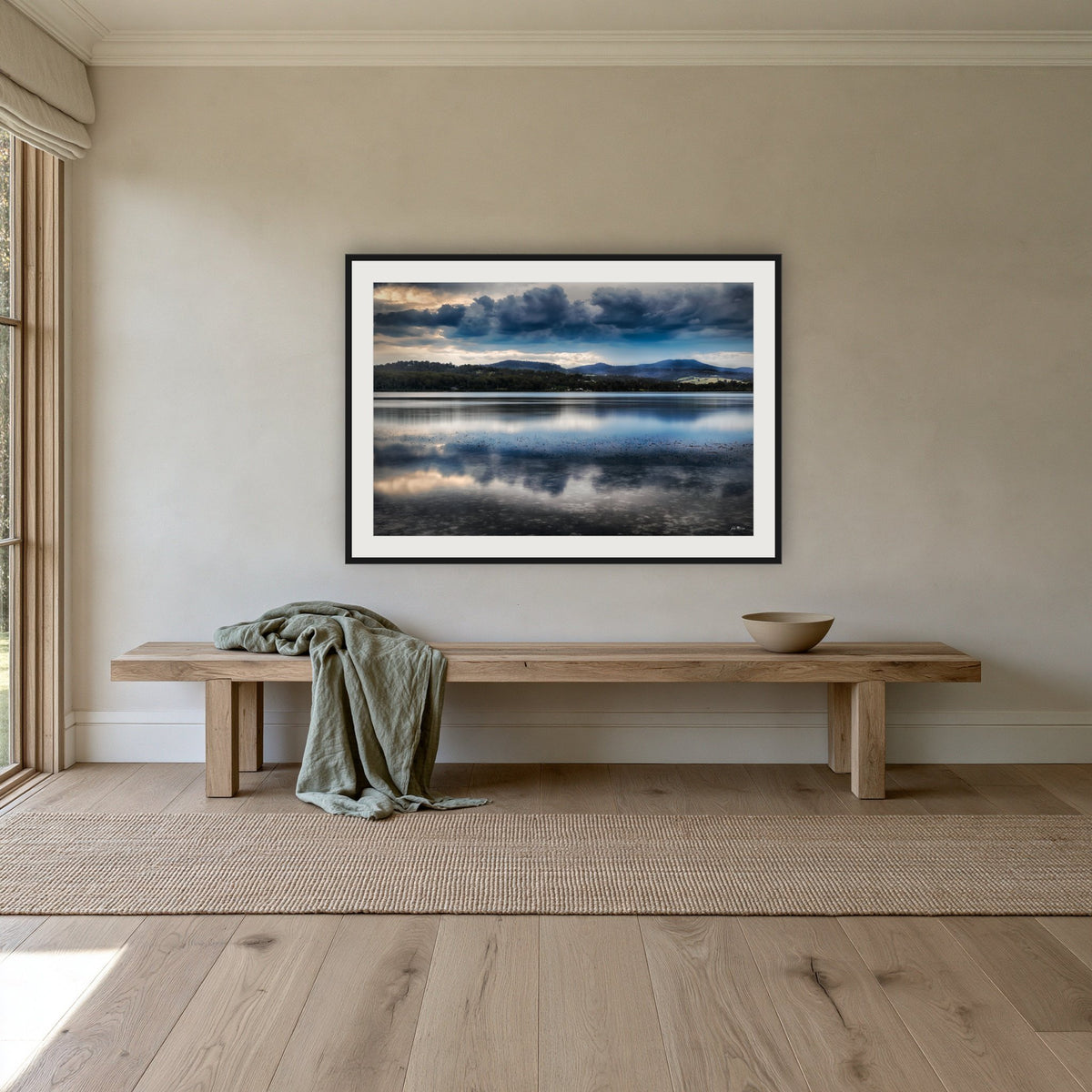 Storm Clouds over Top Lake framed print in black with a white mat, above an oak bench in a hallway