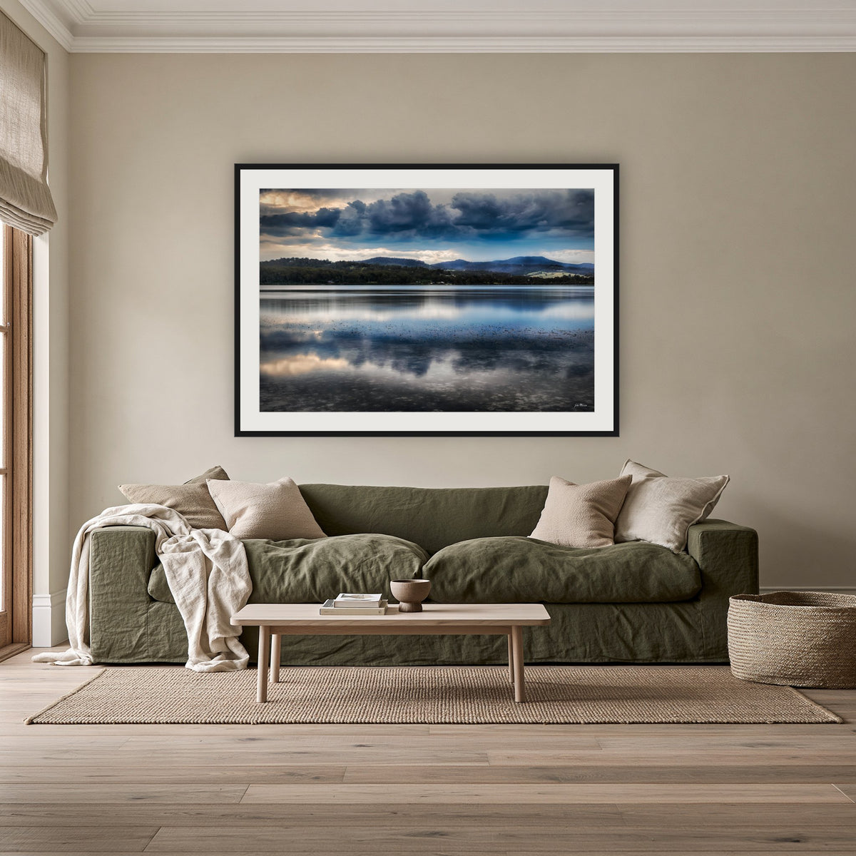 Storm Clouds over Top Lake framed print in black with a white mat, above an olive linen sofa in a lounge room