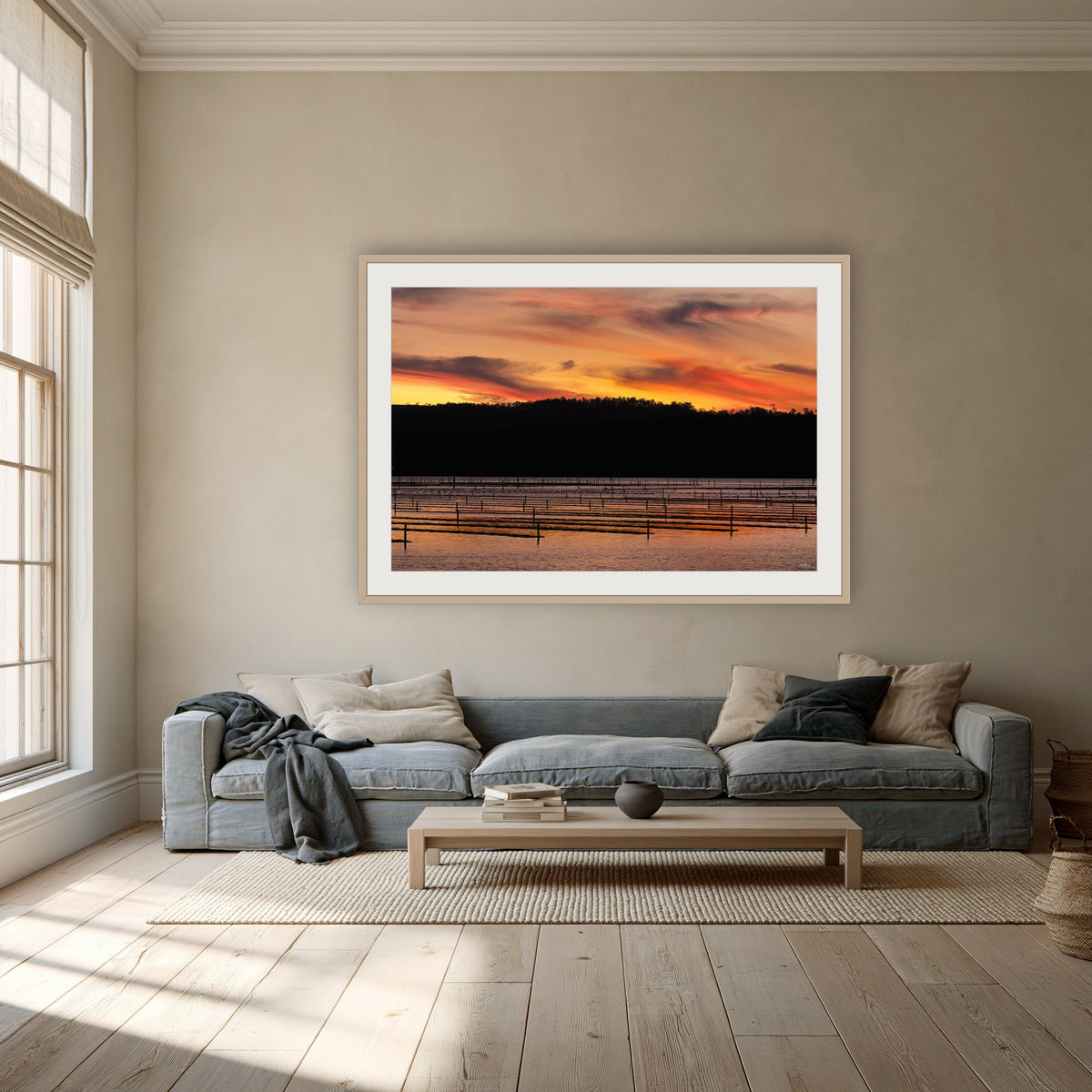 Top Lake Oyster Leases at Sunset framed print in oak with a white mat, above a dusty blue linen sofa in a lounge room