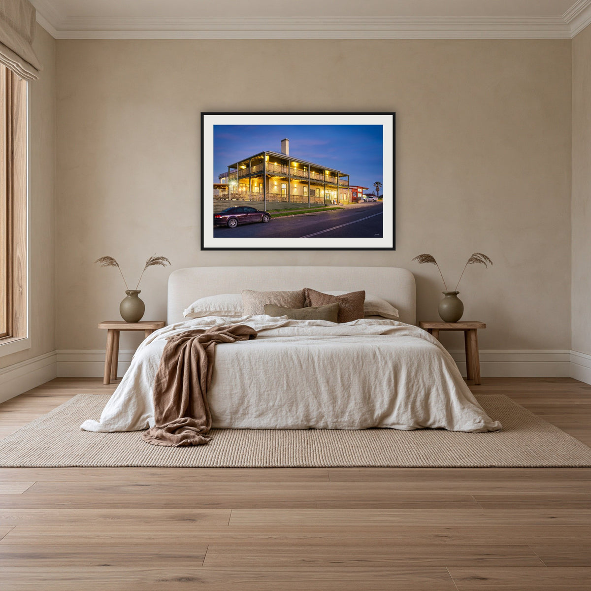 Tathra Hotel framed print in black with a white mat, above an ivory linen bed in a bedroom