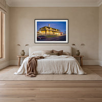 Tathra Hotel framed print in black with a white mat, above an ivory linen bed in a bedroom