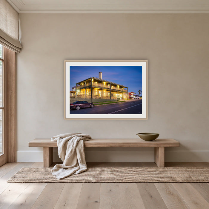 Tathra Hotel framed print in oak with a white mat, above an oak bench in a hallway