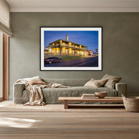 Tathra Hotel framed print in black with a white mat, above a sage linen sofa in a lounge room