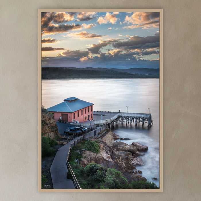 Tathra Wharf Smooth Seas in an oak frame without a mat, in a plaster-walled hallway