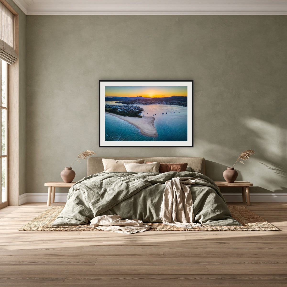 Fishpen Aerial View framed print in black with a white mat, above a khaki linen bed against a green-grey wall in a bedroom
