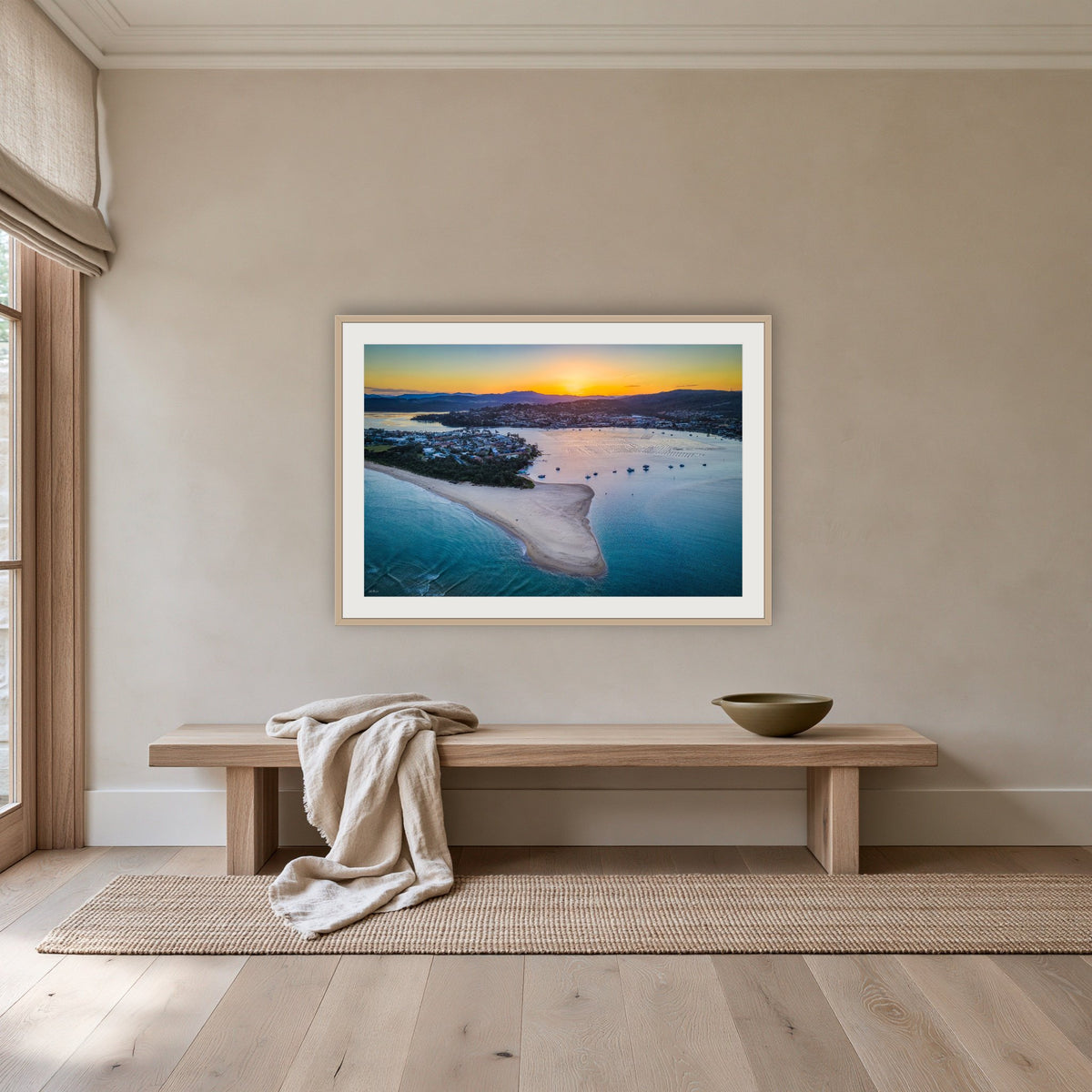 Fishpen Aerial View framed print in oak with a white mat, above an oak bench in a hallway