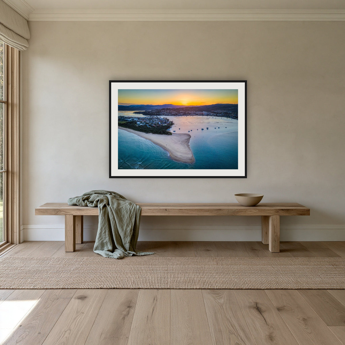 Fishpen Aerial View framed print in black with a white mat, above an oak bench in a hallway