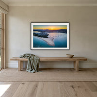 Fishpen Aerial View framed print in black with a white mat, above an oak bench in a hallway