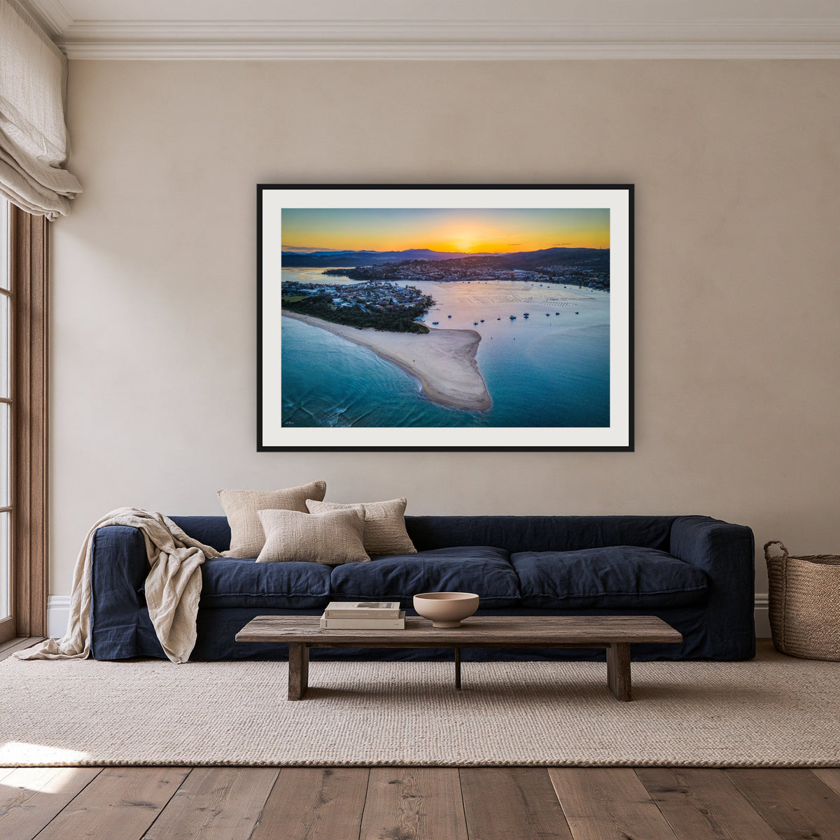 Fishpen Aerial View framed print in black with a white mat, above a navy linen sofa in a lounge room