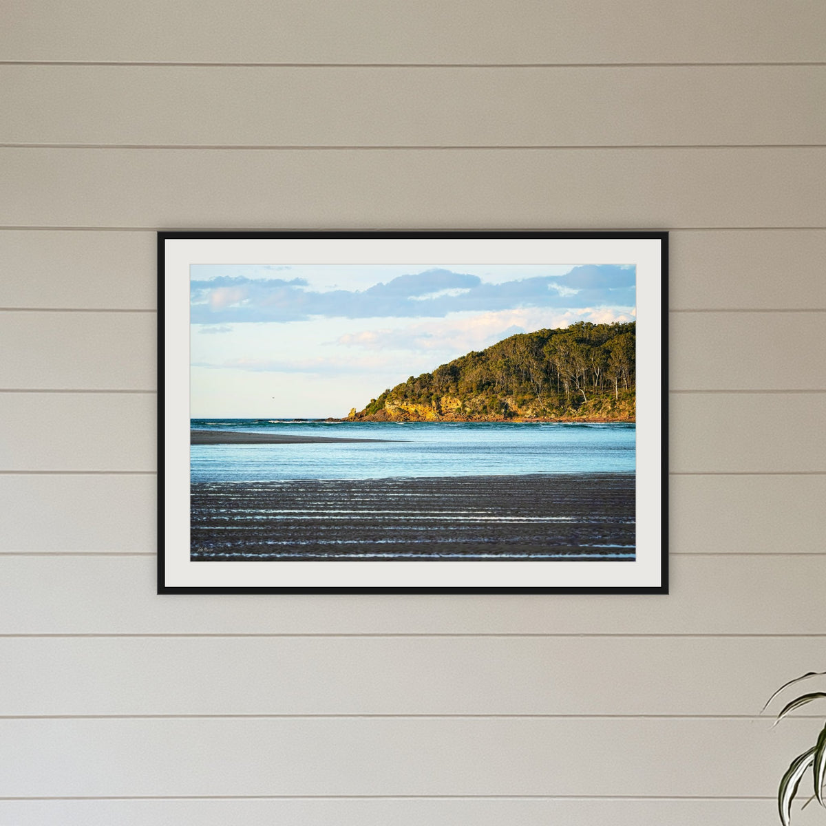 Pambula River Sea Entrance framed print in black with a white mat, above a sofa