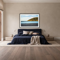 Pambula River Sea Entrance framed print in black with a white mat, above a navy linen bed in a bedroom