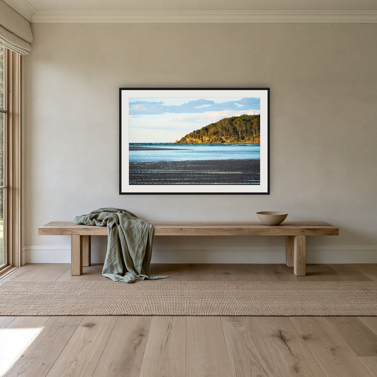Pambula River Sea Entrance framed print in black with a white mat, above an oak bench in a hallway