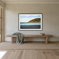Pambula River Sea Entrance framed print in black with a white mat, above an oak bench in a hallway