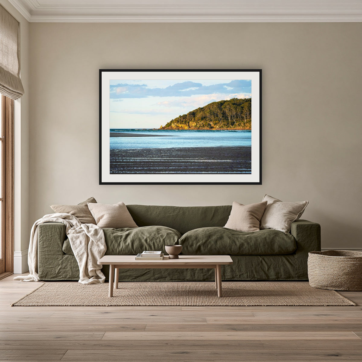 Pambula River Sea Entrance framed print in black with a white mat, above an olive linen sofa in a lounge room