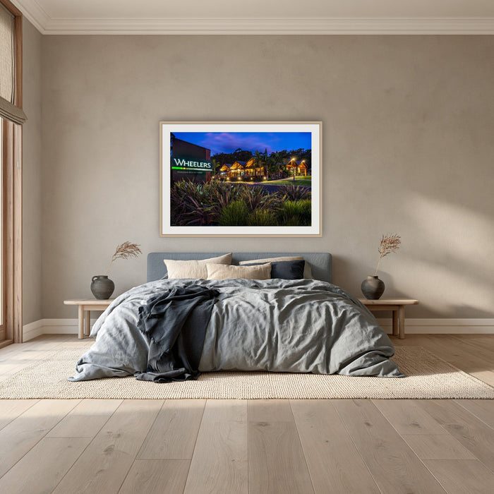 Wheelers Restaurant framed print in oak with a white mat, above a dusty blue linen bed in a bedroom