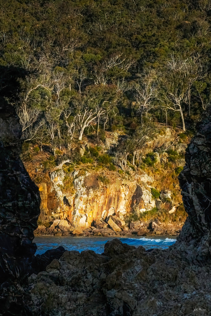 Pambula River seen through a gap in the rocks, white-trunked eucalypts above a sunlit ochre cliff — fine art print