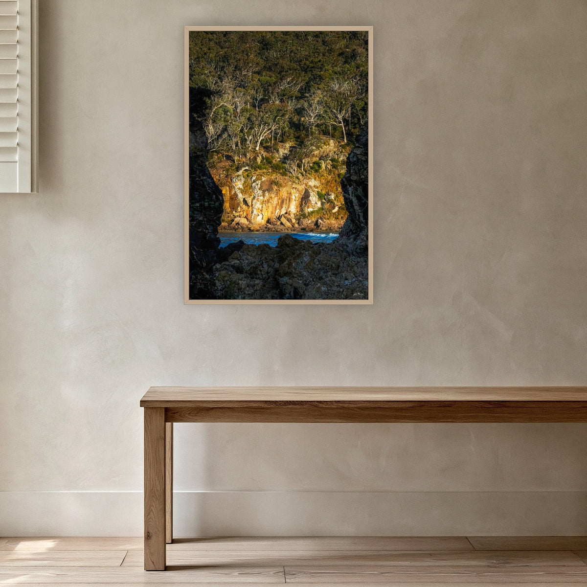 Pambula Beach Rock Frame in an oak frame without a mat, in a plaster-walled hallway