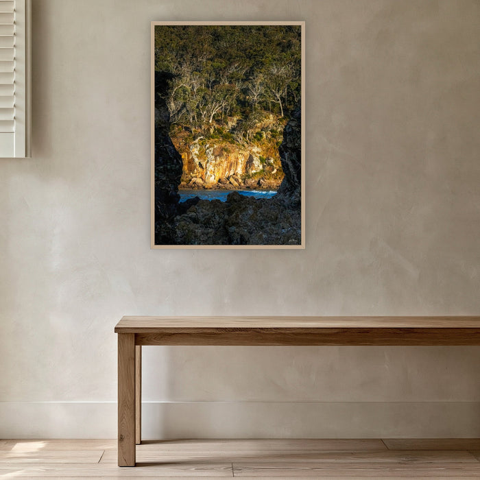 Pambula Beach Rock Frame in an oak frame without a mat, in a plaster-walled hallway