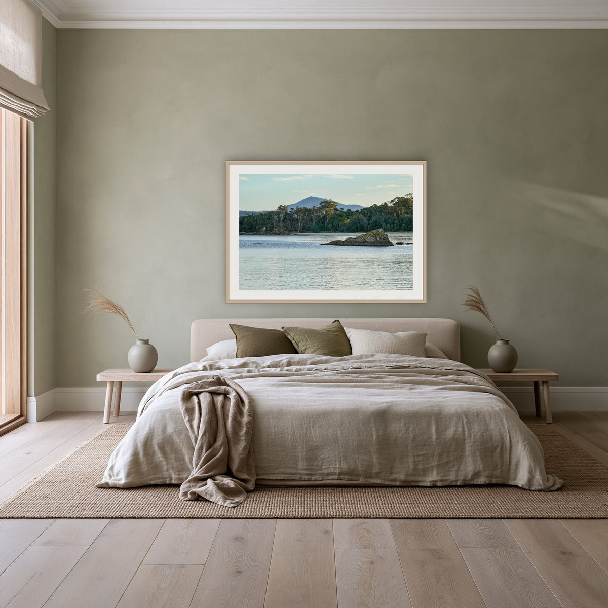 Twofold Bay framed print in oak with a white mat, above a linen bed against a sage wall in a bedroom