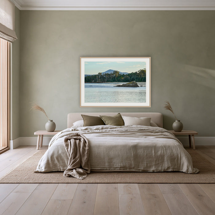 Twofold Bay framed print in oak with a white mat, above a linen bed against a sage wall in a bedroom