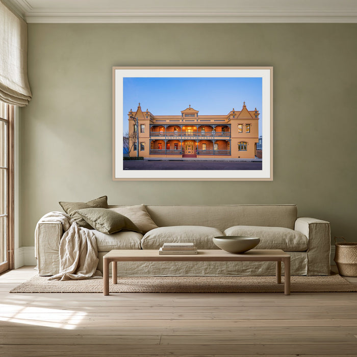 Hotel Australasia framed print in oak with a white mat, above a linen sofa against a sage wall in a lounge room