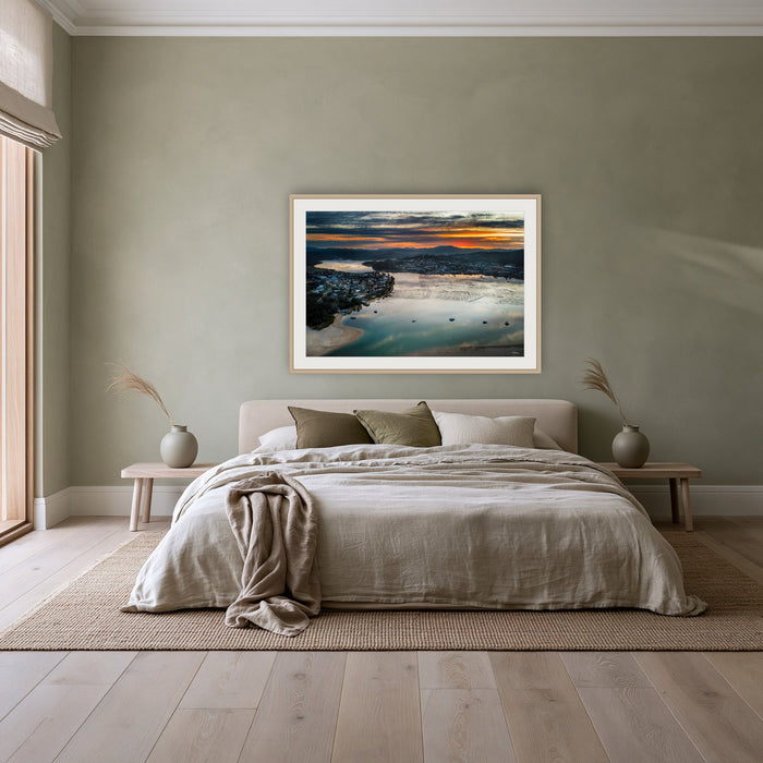 Merimbula Eagle Eye Sunset framed print in oak with a white mat, above a linen bed against a sage wall in a bedroom