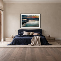 Merimbula Eagle Eye Sunset framed print in black with a white mat, above a navy linen bed in a bedroom