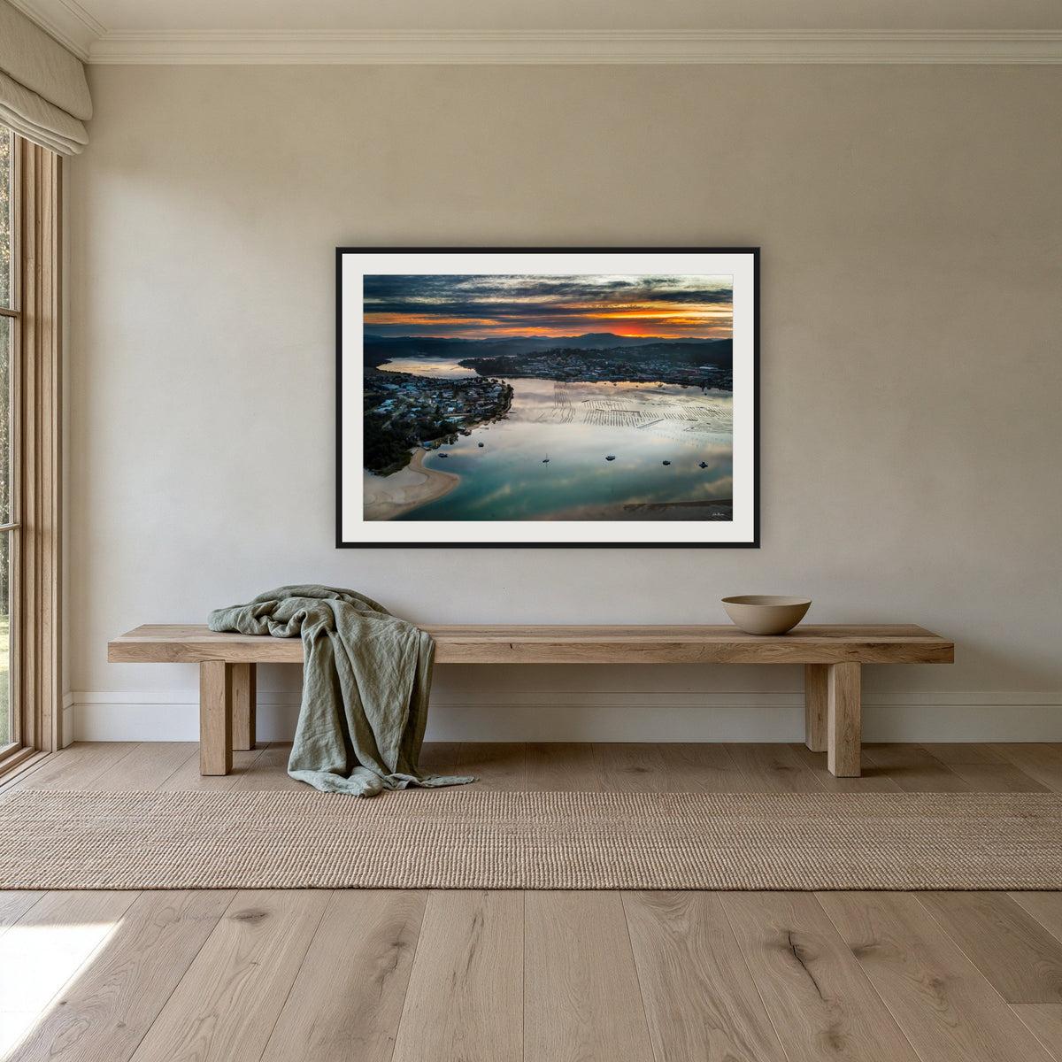 Merimbula Eagle Eye Sunset framed print in black with a white mat, above an oak bench in a hallway