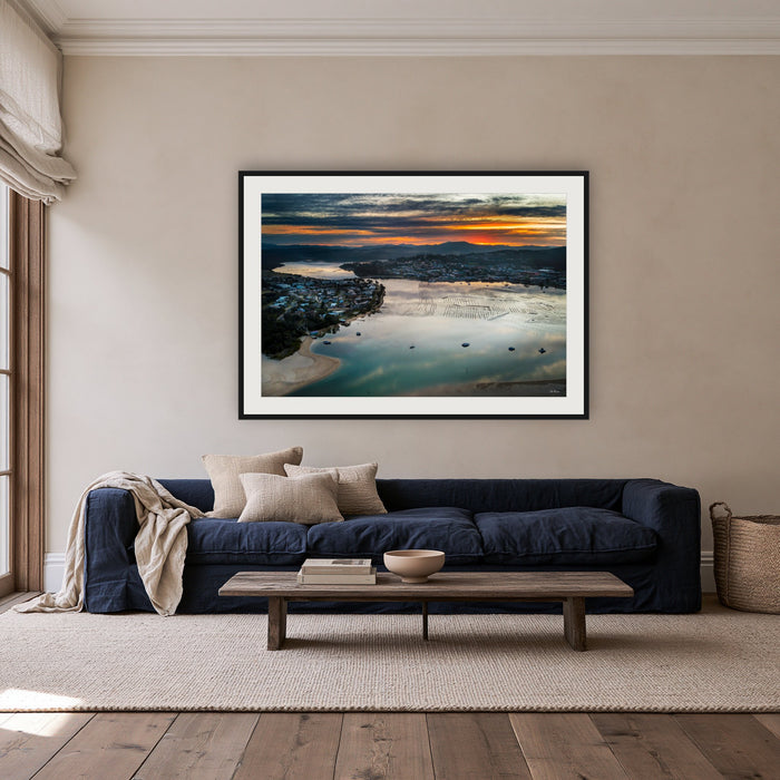 Merimbula Eagle Eye Sunset framed print in black with a white mat, above a navy linen sofa in a lounge room