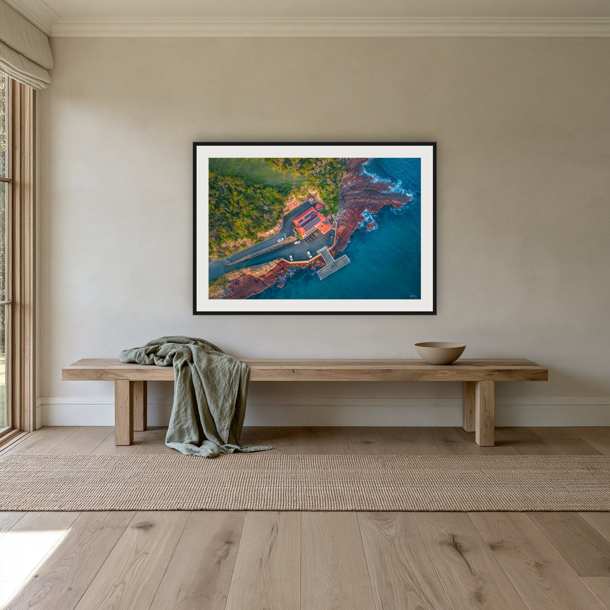 Merimbula Wharf framed print in black with a white mat, above an oak bench in a hallway