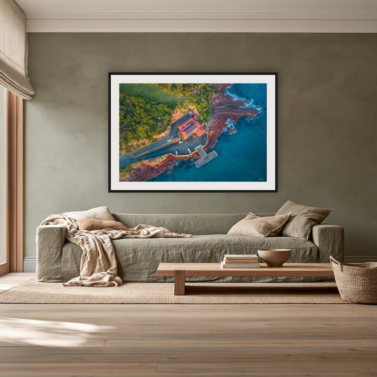 Merimbula Wharf framed print in black with a white mat, above a sage linen sofa in a lounge room