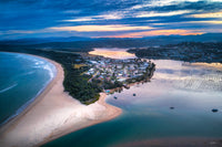 Aerial view at dusk of the Fishpen peninsula at Merimbula, houses among the trees with the ocean beach curving away on one side and the lake and oyster leases on the other — fine art print