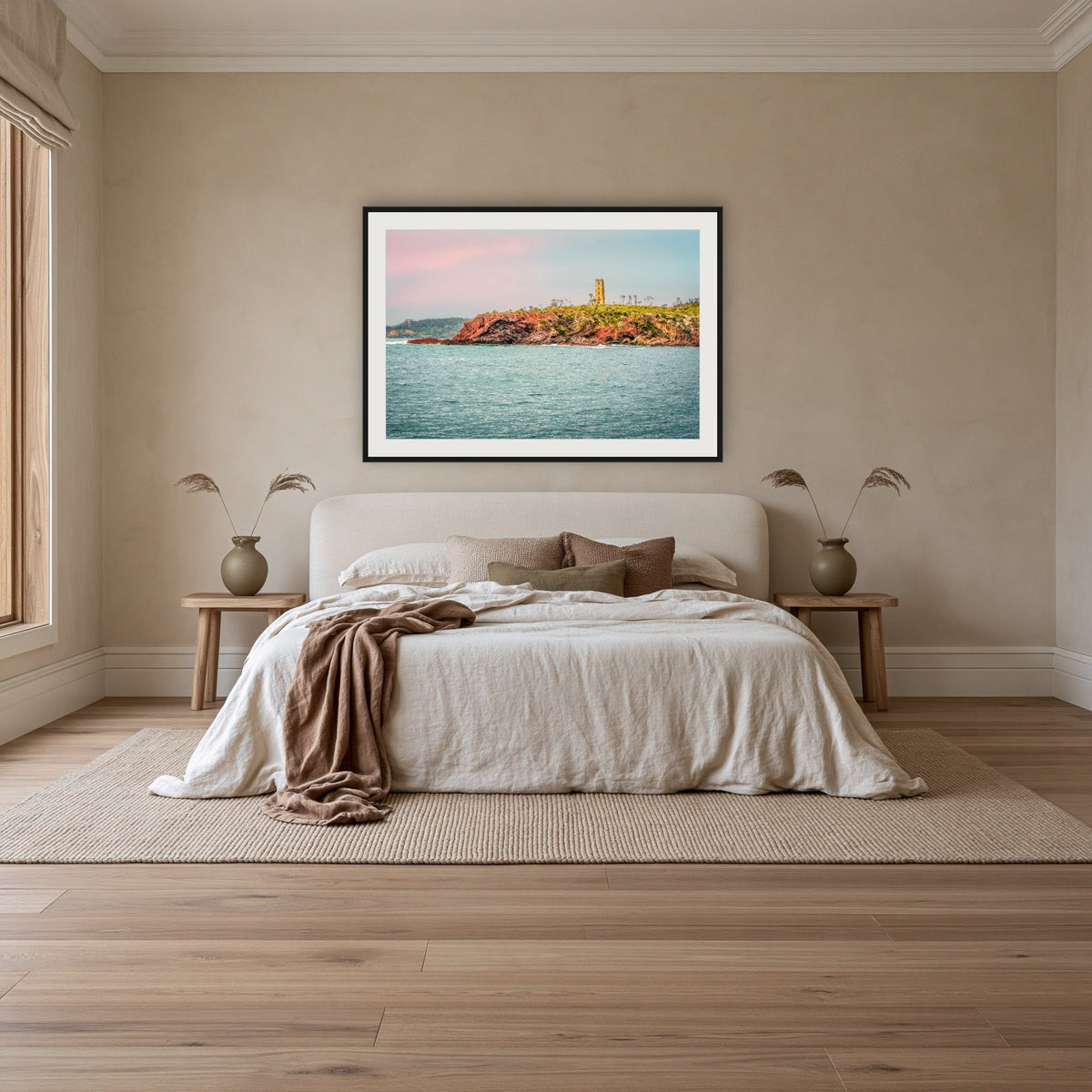 Ben Boyd Tower Seascape framed print in black with a white mat, above an ivory linen bed in a bedroom