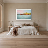 Ben Boyd Tower Seascape framed print in black with a white mat, above an ivory linen bed in a bedroom