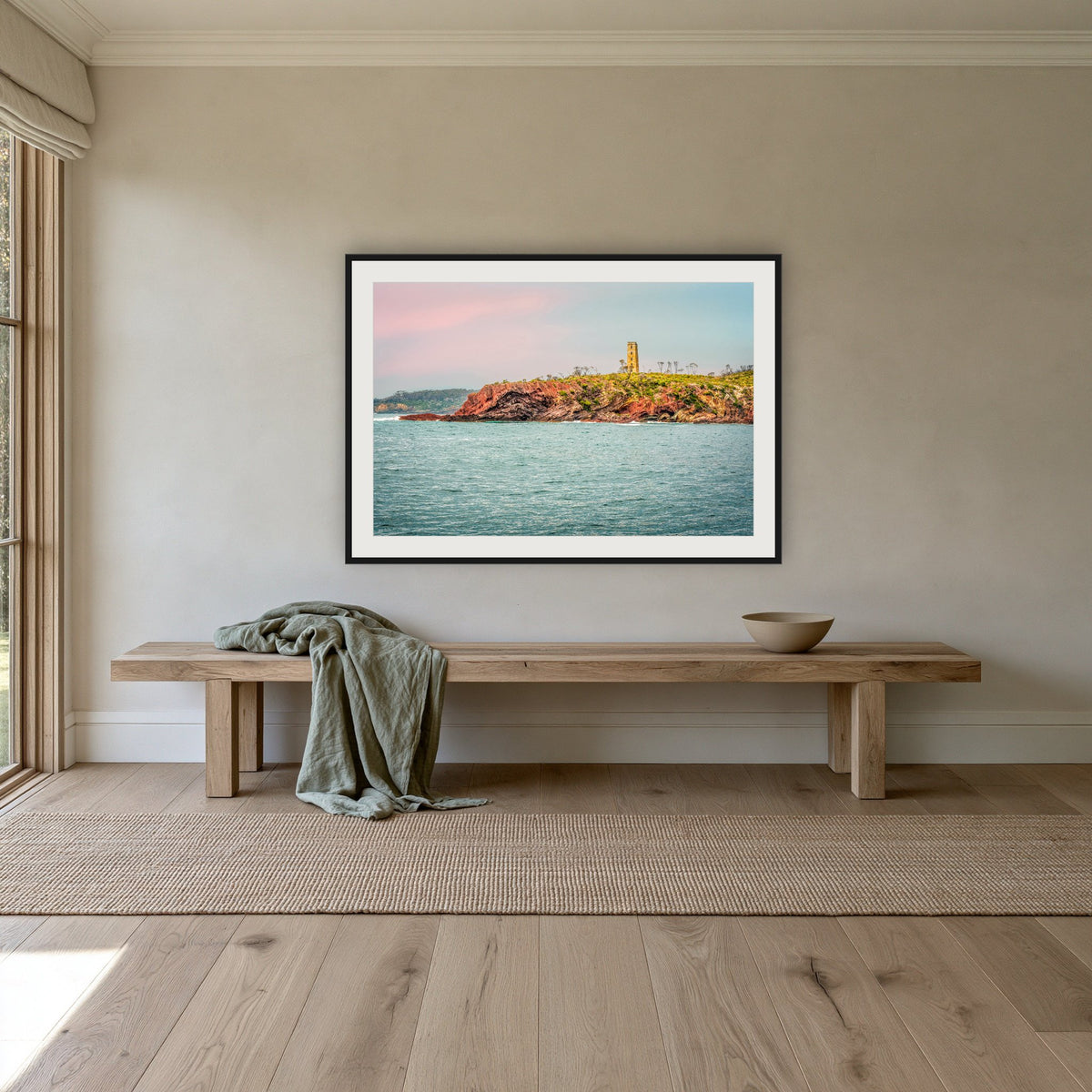 Ben Boyd Tower Seascape framed print in black with a white mat, above an oak bench in a hallway