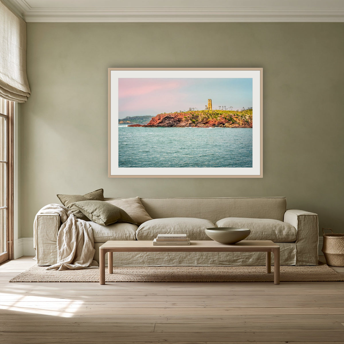 Ben Boyd Tower Seascape framed print in oak with a white mat, above a linen sofa against a sage wall in a lounge room