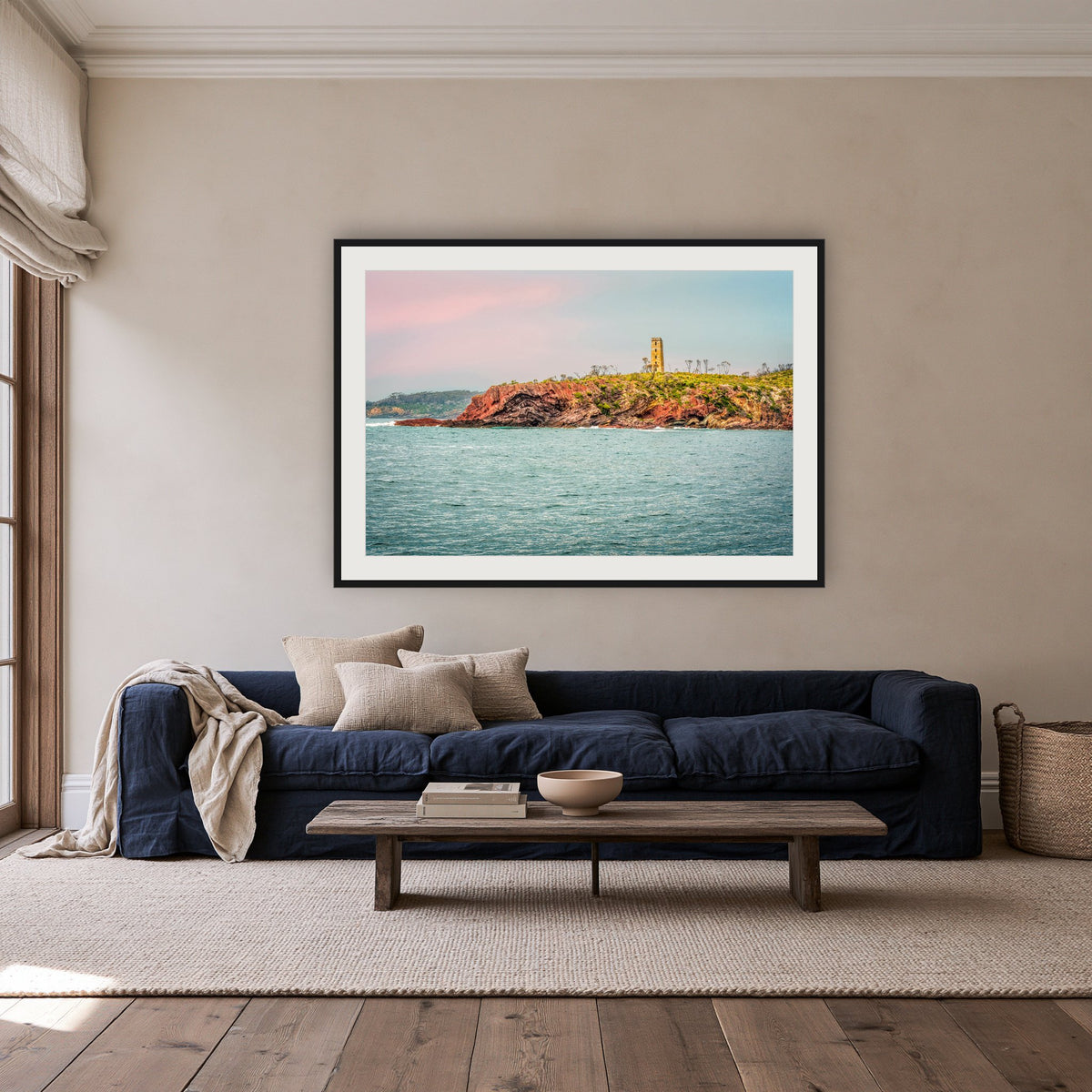 Ben Boyd Tower Seascape framed print in black with a white mat, above a navy linen sofa in a lounge room