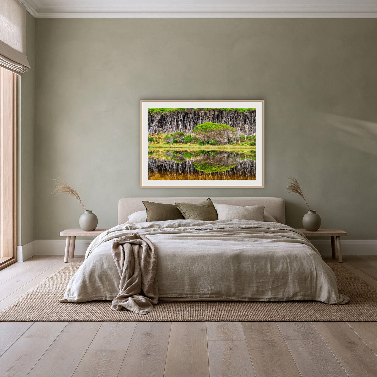 Bournda Lagoon Reflections framed print in oak with a white mat, above a linen bed against a sage wall in a bedroom