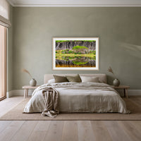 Bournda Lagoon Reflections framed print in oak with a white mat, above a linen bed against a sage wall in a bedroom