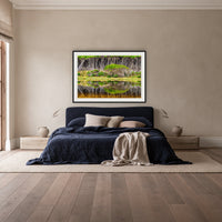 Bournda Lagoon Reflections framed print in black with a white mat, above a navy linen bed in a bedroom